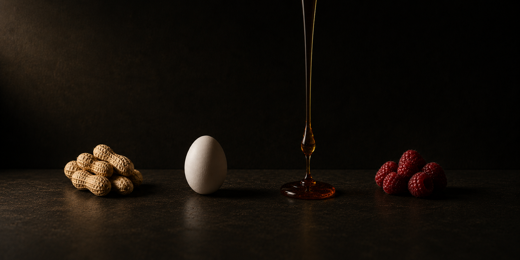 Four ingredients on a dark surface: peanuts, an egg, a stream of maple syrup, and raspberries